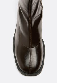 Bottine en cuir marron avec une finition lisse, fermeture éclair sur le côté, coutures contrastantes et une semelle en caoutchouc noir basse.