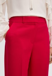 Rode getailleerde broek met een gladde textuur, voorzien van zijzakken en een rechte pijpdesign. Draagt men met een witte blouse.