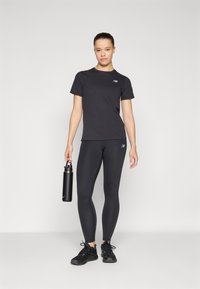 T-shirt de sport noir et legging au design ajusté, tenant une bouteille d'eau noire. Comprend des accents réfléchissants et des détails de logo.