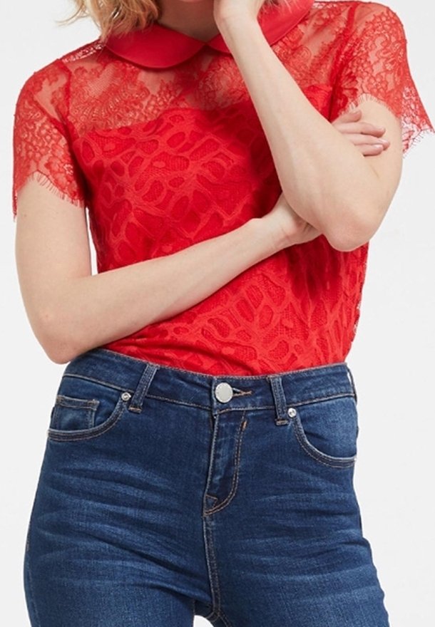 Blusa de encaje rojo con un cuello sólido, que presenta una textura estampada, combinada con jeans de mezclilla azul oscuro de cintura alta.