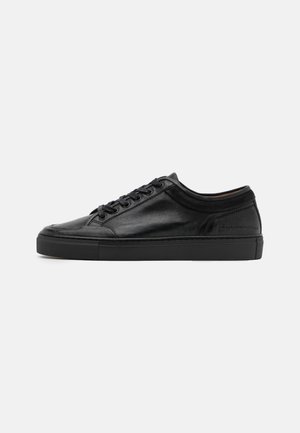 Sort lavtsiddende læder sneaker med snørebånd foran og tekstureret gummisål, vist i sideprofil på ensfarvet baggrund.