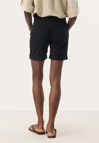 Svarta shorts med uppvikta ärmar, tillverkade av ett lätt material, med en minimalistisk design. Slät textur med två bakfickor.