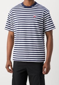 Marineblå og hvid stribet t-shirt med korte ærmer, rund halsudskæring og et lille rødt broderet logo på venstre bryst. Lavet af blødt stof.