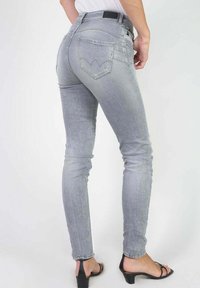 Jean gris ajusté avec une taille haute, légèrement extensible, et des poches arrière avec un design incurvé. Une paire de sandales à talons noires complète le look.