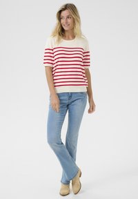 Pull en tricot rayé rouge et blanc à manches courtes, associé à un jean flare bleu clair et des bottines crème.