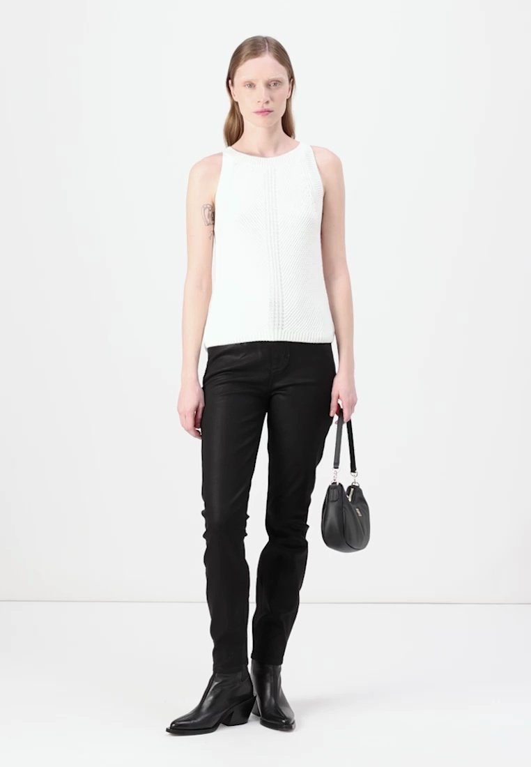 Haut tricot sans manches blanc avec un motif texturé, associé à un jean noir ajusté et des bottes à talons noires. Petit sac à main noir à la main.