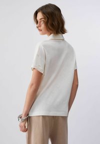 Polo couleur crème avec une coupe décontractée, manches courtes et texture douce. Col plat distinctif au niveau de l'encolure.