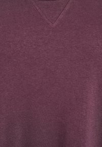 Prikaz izbliza bordo tkanine koja pokazuje finu pletenu teksturu i prošiveni V-izrez na vratu.