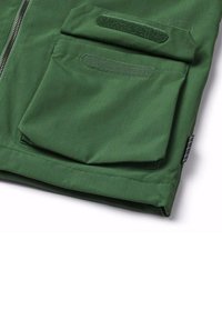 Groene stoffen jas met ritssluiting, voorzien van een grote zak en een klittenbandflap op de linker mouw, gestructureerd oppervlak met een ruitpatroon.