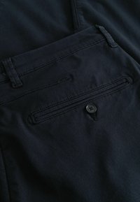 Sötétkék nadrág texturált anyagból, hátsó zsebbel, gombos záródással és lapos derékpánttal.