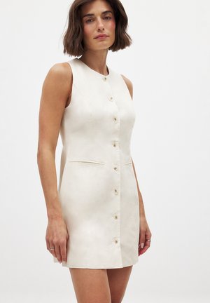 Vestido sin mangas hasta la rodilla de tela beige claro con un cierre frontal de botones, dos bolsillos laterales y costuras verticales sutiles.