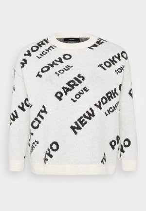 Bijela pletena majica s oversized crnim natpisima gradova, poput "PARIZ" i "TOKIO", s okruglim izrezom i rebrastim manžetama.