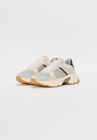 Sneakerid, mis on valmistatud heledast beežist, helesinist ja tumesinist nubuk- ja võrkmaterjalist, millel on mahukas valge tald ja tekstureeritud kummi põhi.