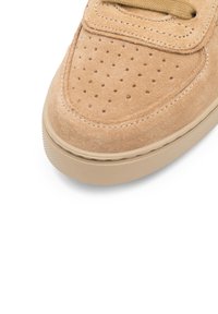 Zapatillas de ante beige con detalles perforados, puntera redondeada y suela de goma texturizada. Área de cordones suave con acentos cosidos.