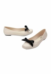 Bailarinas en suave material beige con puntera redondeada, que presentan un lazo negro texturizado y un bajo tacón negro.