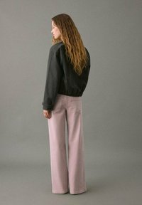 Chaqueta negra corta de manga larga combinada con pantalones de pierna ancha en rosa claro. Textura de tela suave, diseño minimalista y sin patrones visibles.