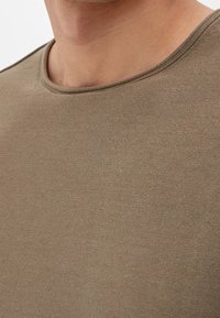 T-shirt in cotone verde oliva con collo a giro, caratterizzato da un tessuto testurizzato e dettagli di cucitura sottili lungo i bordi.