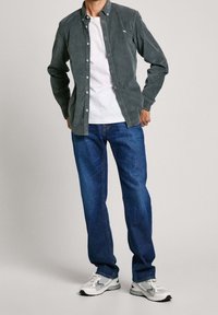 Camicia button-up in corduroy grigia sopra una maglietta bianca, abbinata a jeans blu e scarpe da corsa grigie con accenti bianchi.