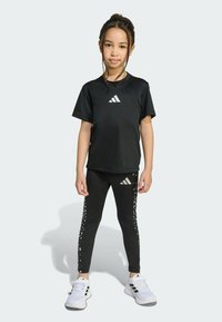 Black athletic outfit featuring a short-sleeve t-shirt and fitted leggings with a dotted design. White logo accents on both pieces. Sneakers are white.