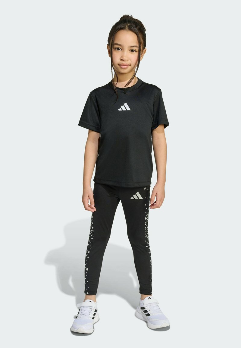 Black athletic outfit featuring a short-sleeve t-shirt and fitted leggings with a dotted design. White logo accents on both pieces. Sneakers are white.