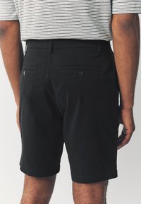 Zwarte katoenen shorts met een gladde textuur, voorzien van achterzakken met knoopsluitingen en een rechte pasvorm, gecombineerd met een gestreept overhemd.