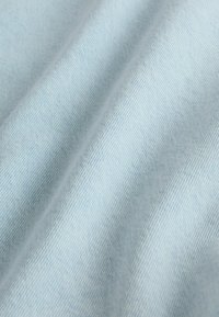 Tissu en denim bleu clair avec une texture de tissage diagonal visible et des plis doux créant de légères ombres.