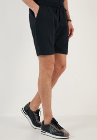 Shorts bleumarin cu o textură ribbed, prevăzuți cu un talie elastică, buzunare laterale și o croială relaxată. Asortați cu adidași închisi la culoare.