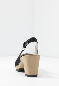 Mörkblåmocka högklackad sandal med justerbar ankelrem, träblockklack och texturerad yttersula. Minimalistisk design, bakvy.