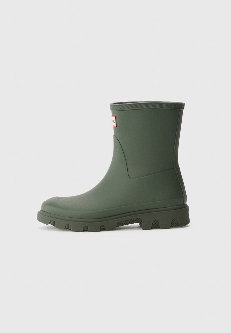 Botte de cheville en caoutchouc vert avec une texture lisse, un haut revers et une semelle robuste. Présente un petit logo sur le côté et un embout arrondi.