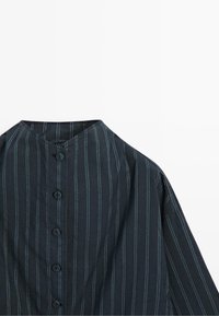 Schwarzes Hemd mit Knopfleiste, blauen vertikalen Streifen und rundem Ausschnitt, flach auf weißem Hintergrund ausgelegt.