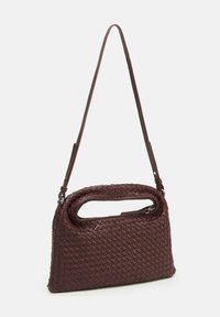 Sac à main tissé bordeaux avec une surface texturée, une découpe arrondie pour la poignée et une bandoulière réglable. Comprend une fermeture zippée.
