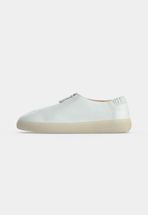 Chaussure blanche à profil bas, enfilable, avec un embout arrondi, une semelle beige, un détail élastique à l’arrière et une fermeture éclair sur le dessus.