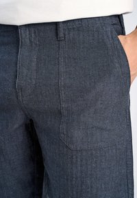 Mörkblå byxor med fiskbensmönster och sidofickor. Tillverkade av textil med struktur, med en rak ben-design.