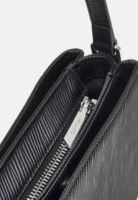 Borsa nera con superficie texturizzata e a righe, zip argentata e rivestimento in tessuto. Progettata con una spallina unica e molteplici scomparti.