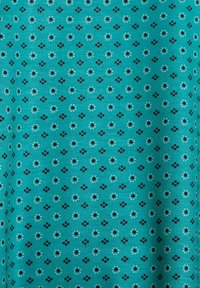 Tissu turquoise avec un motif floral répétitif comprenant de petites fleurs noires et blanches et de minuscules points, le tout sur un fond texturé.