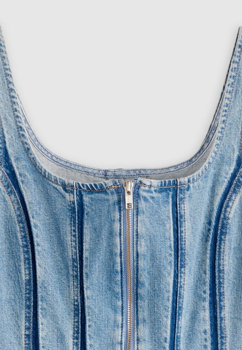 Denimkjole med rundet halsudskæring, lyseblåt stof, lodrette syninger og en central lynlåsdetalje. Tekstureret overflade med en let falmet finish.