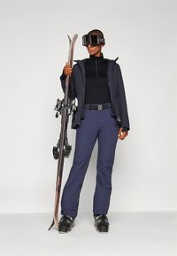 Smučarski komplet, ki vključuje črno jakno na zadrgo, črno majico in temno modre smučarske hlače. Opremljen z zaščitnimi očali za smučanje in drži smuči z vezmi.