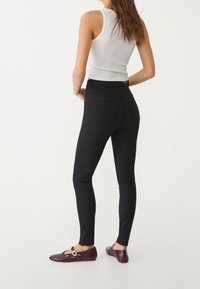 Černé skinny džíny z denimu, s vysokým pasem, úzkým střihem a surovým lemem. V kombinaci s bílým tílkem a vínovými mokasíny.