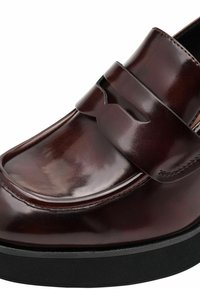 Mocasín de cuero marrón con un acabado brillante, una banda decorativa sobre el empeine y una suela texturada negra, con contornos suaves y detalles de costura.