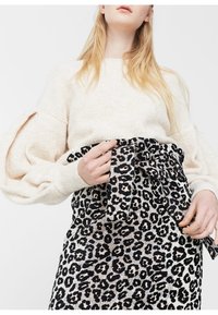Suéter texturizado color crema con mangas globo, combinado con una falda ajustada que presenta un audaz estampado de leopardo en negro y crema, con detalle de lazo.