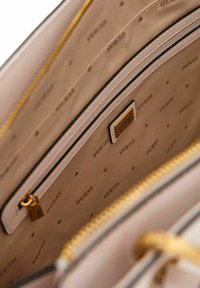 Interno rosa con tessuto beige, caratterizzato da un motivo ripetuto del logo "Guess", tasca con zip e dettagli in hardware dorato.