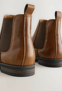 Botas Chelsea de cuero marrón con paneles elásticos en los laterales, punteras redondeadas y tiradores. Presenta una suela de goma negra texturizada.