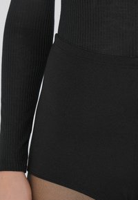Zwart geribbeld bodysuit met lange mouwen en een slim fit taille, met een gladde, doorschijnende tan panel aan de onderkant. Zacht, rekbaar materiaal.