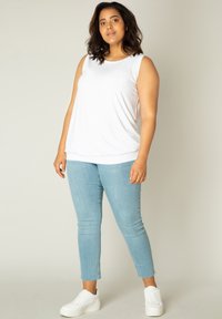 Witte mouwloze top van zachte stof, gecombineerd met lichtblauwe skinny jeans met een rafelrand en witte sneakers. Eenvoudige, casual outfit.