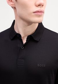 Black polo shirt made of smooth fabric features a collar, two-button placket, and a subtle embossed "BOSS" logo on the chest.