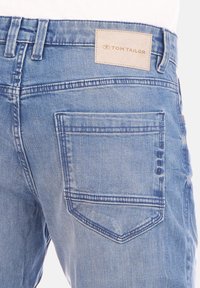 Vaqueros de denim en azul claro con un acabado texturizado, que cuentan con un bolsillo trasero y una etiqueta de tela en color marrón claro, grabada con "TOM TAILOR."