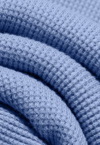 Tissu tricoté bleu clair doux avec une texture côtelée plié en couches superposées.