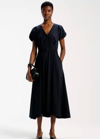 Obleka brez rokavov, dolžine do kolen v mornarsko modri barvi z V-izrezom, nabranimi rameni in poudarjenim pasom, kombinirana z majhno črno torbico. Široka, tekoča krila.