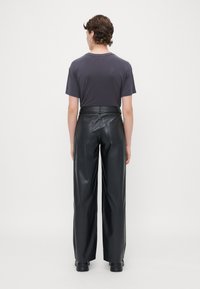 Pantalons larges en cuir noir avec poches arrières, associés à un t-shirt court et ajusté de couleur gris foncé. Le tissu est lisse et brillant.