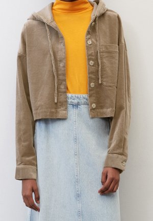 Persoon draagt een cropped beige corduroy jas over een felgele coltrui en een lichtblauwe high-waisted denim rok.